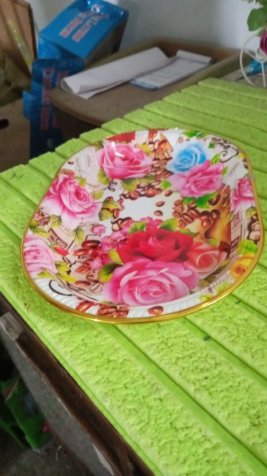 An oval white tray with a pink and red rose pattern and coffee bean accents, on a textured green surface.