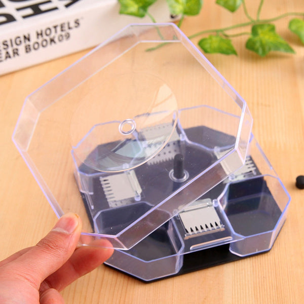 A hand lifting the clear lid of an octagonal cockroach trap on a wooden surface next to a book.