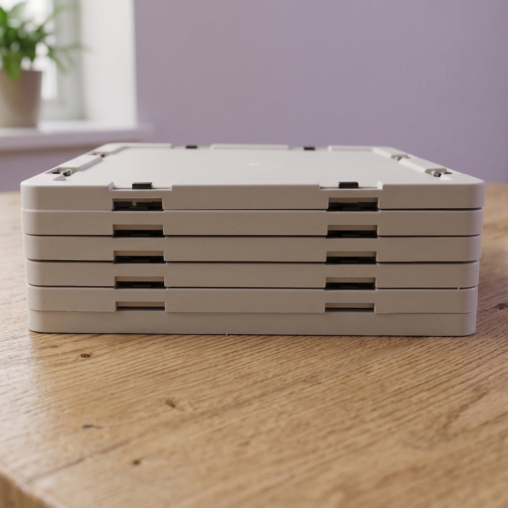 A close-up side view of the shoe rack collapsed into a stack of four flat, light grey panels on a wooden surface.