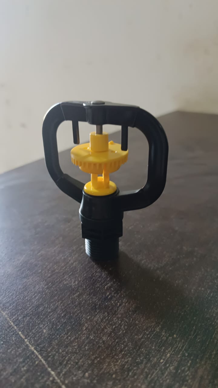 A black and yellow rotating sprinkler nozzle resting on a dark brown surface.