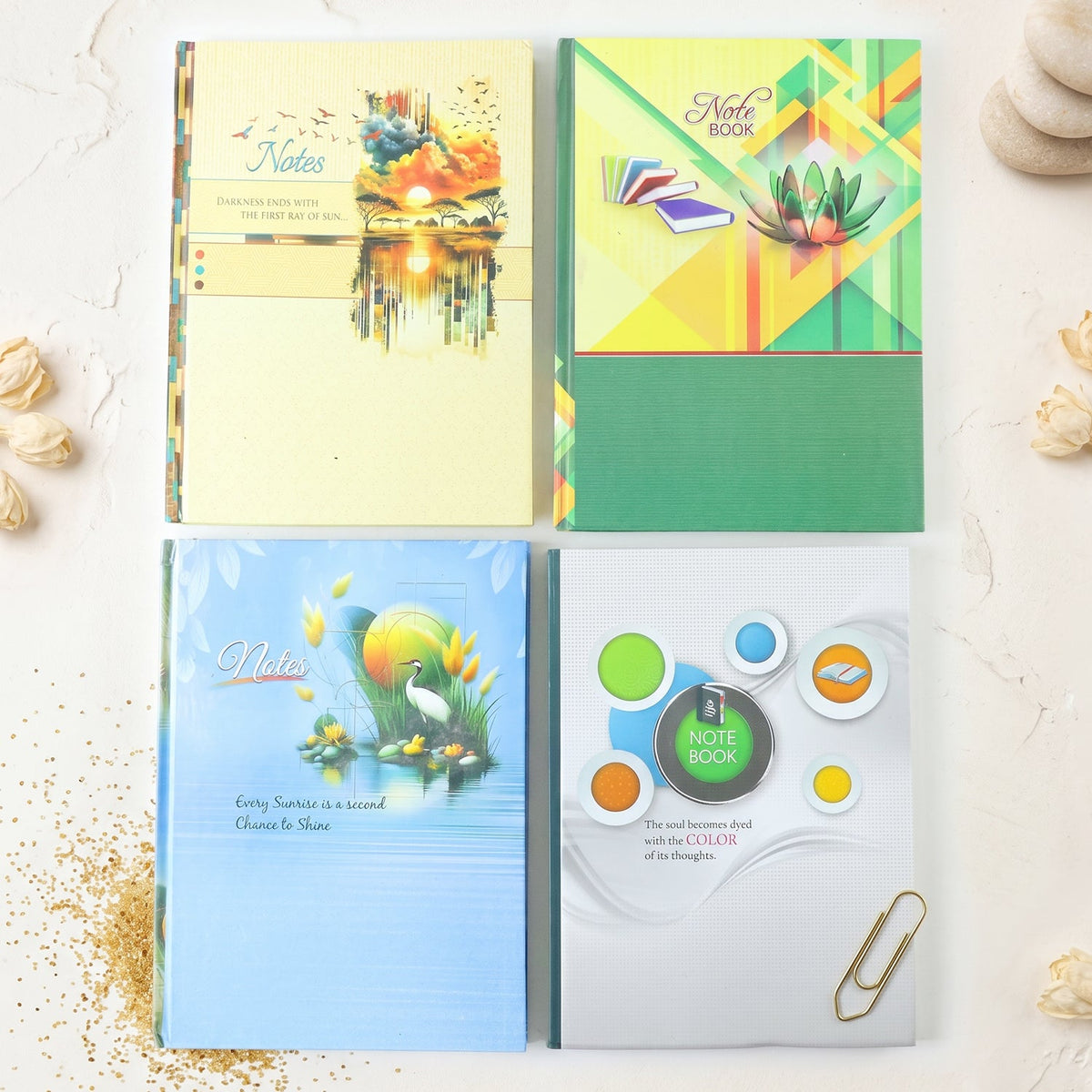 Four different hardbound ruled notebooks with colorful covers, arranged on a white surface with decorative elements.