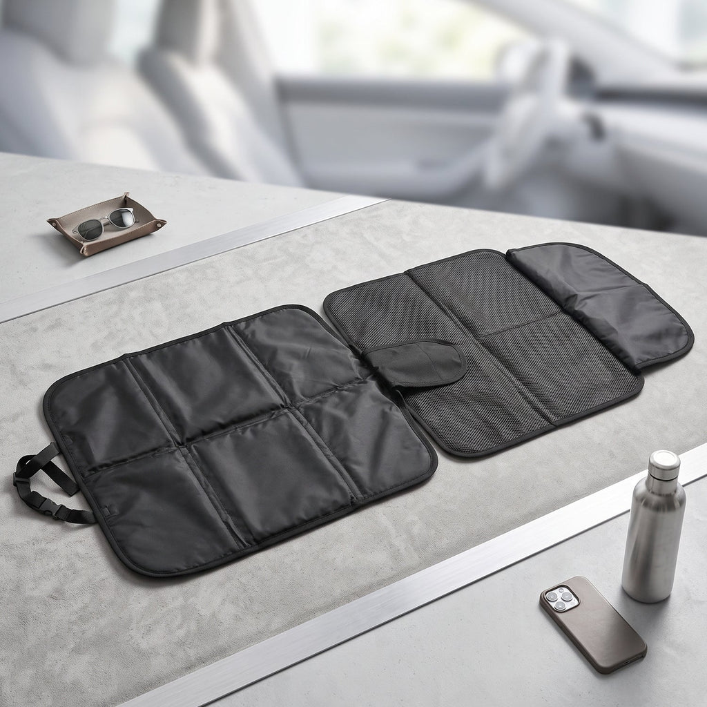 The black car seat protector is unfolded on a gray surface, displaying its padded and mesh sections.