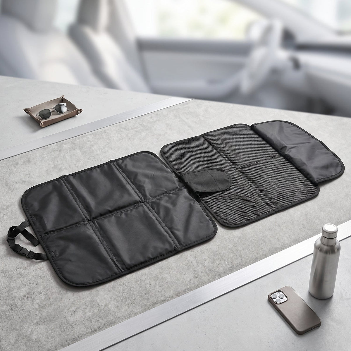 The black car seat protector is unfolded on a gray surface, displaying its padded and mesh sections.