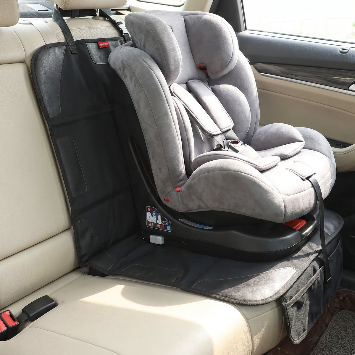 A gray child's car seat is positioned on a black protector in a beige car interior.