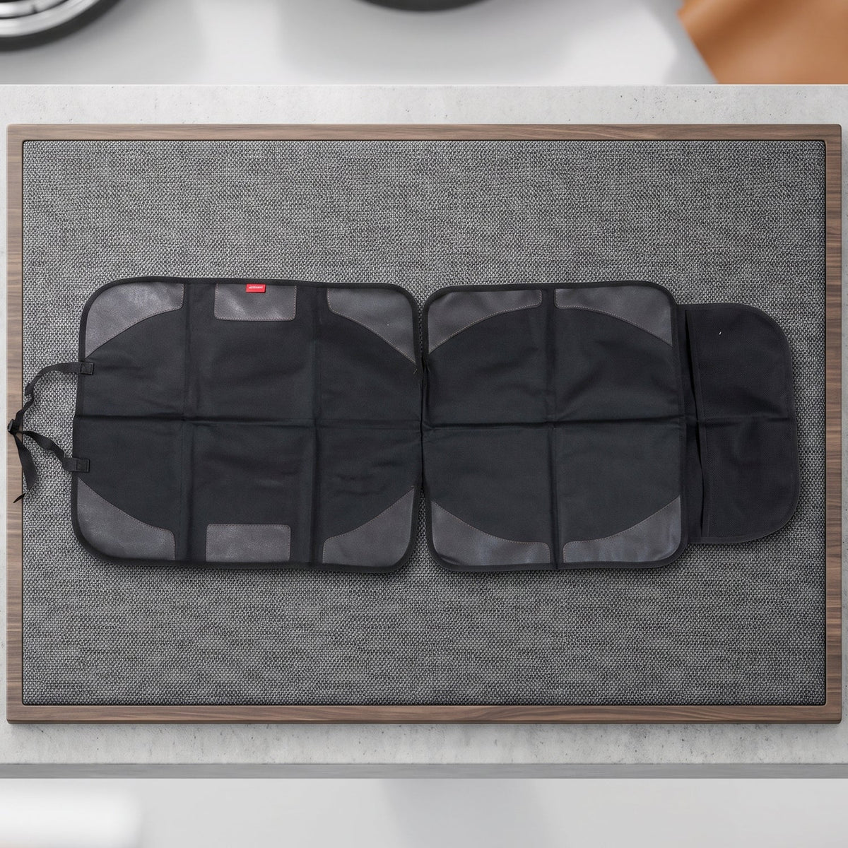 The black car seat protector is spread out on a textured gray mat with a wooden border.