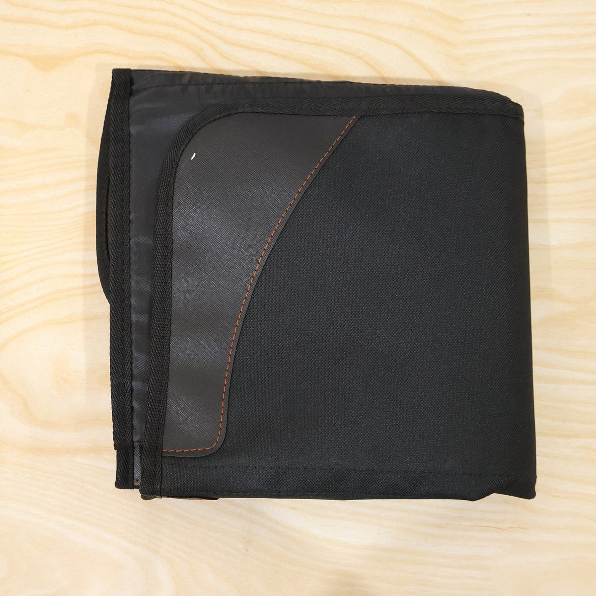 The black car seat protector is neatly folded into a compact square on a light wooden surface.