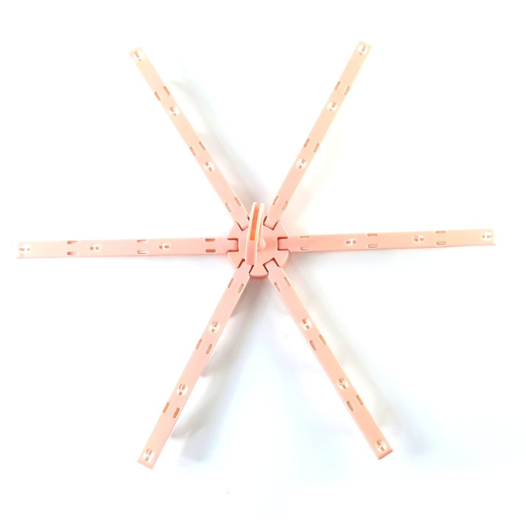 A pink plastic foldable clothes drying rack, unfolded in a star shape, is centered on a white background.