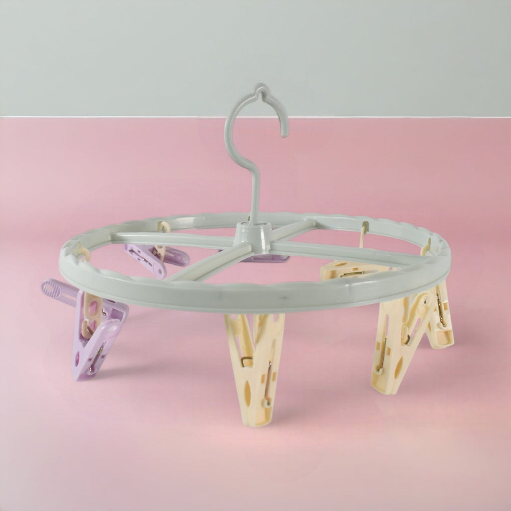 A light blue circular drying rack with purple and yellow clips is centered on a pink and grey background.