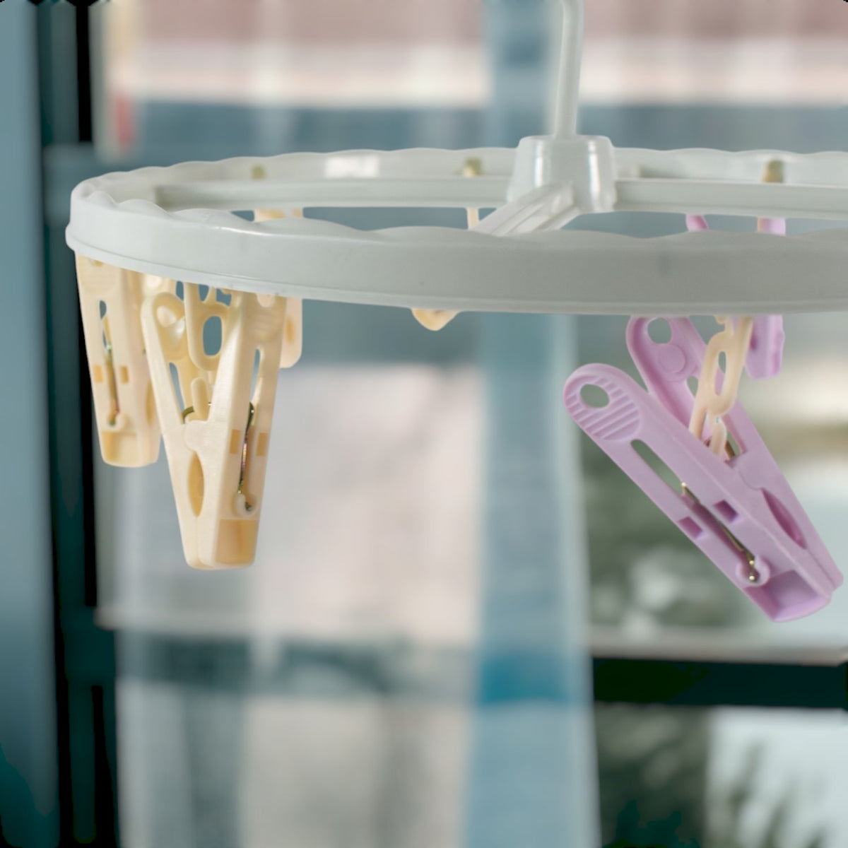 Close-up of a light blue circular drying rack with yellow and purple clips, with a window in the background.