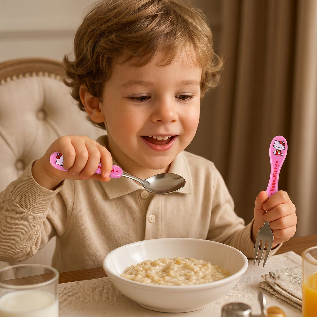 A young boy happily eating with a pink Hello Kitty spoon and fork.