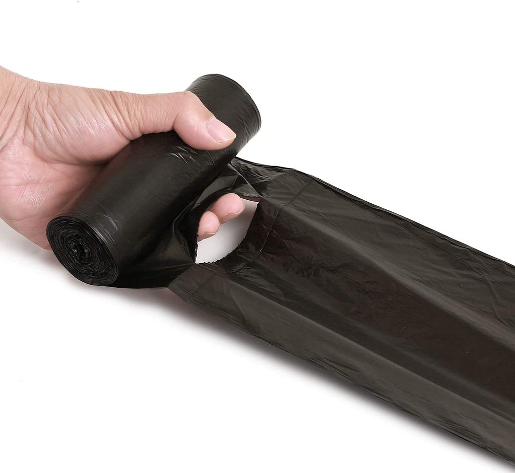 A hand holding a roll of black garbage bags, pulling one bag off the roll.