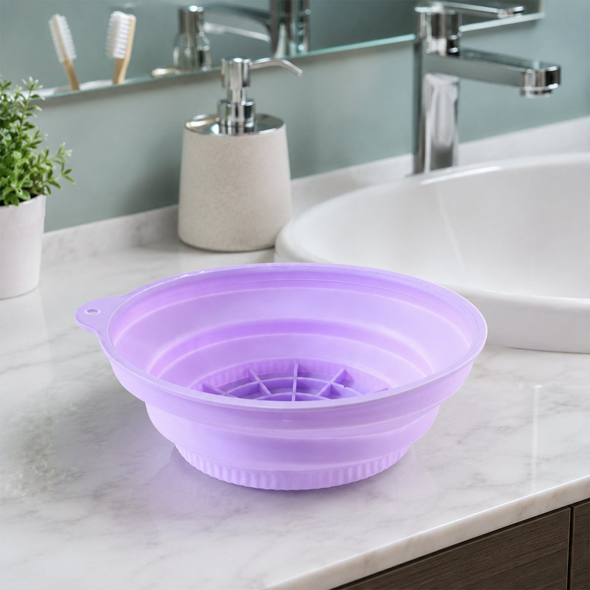 A purple collapsible silicone bowl with a grid pattern sits on a marble bathroom counter next to a sink and soap dispenser.