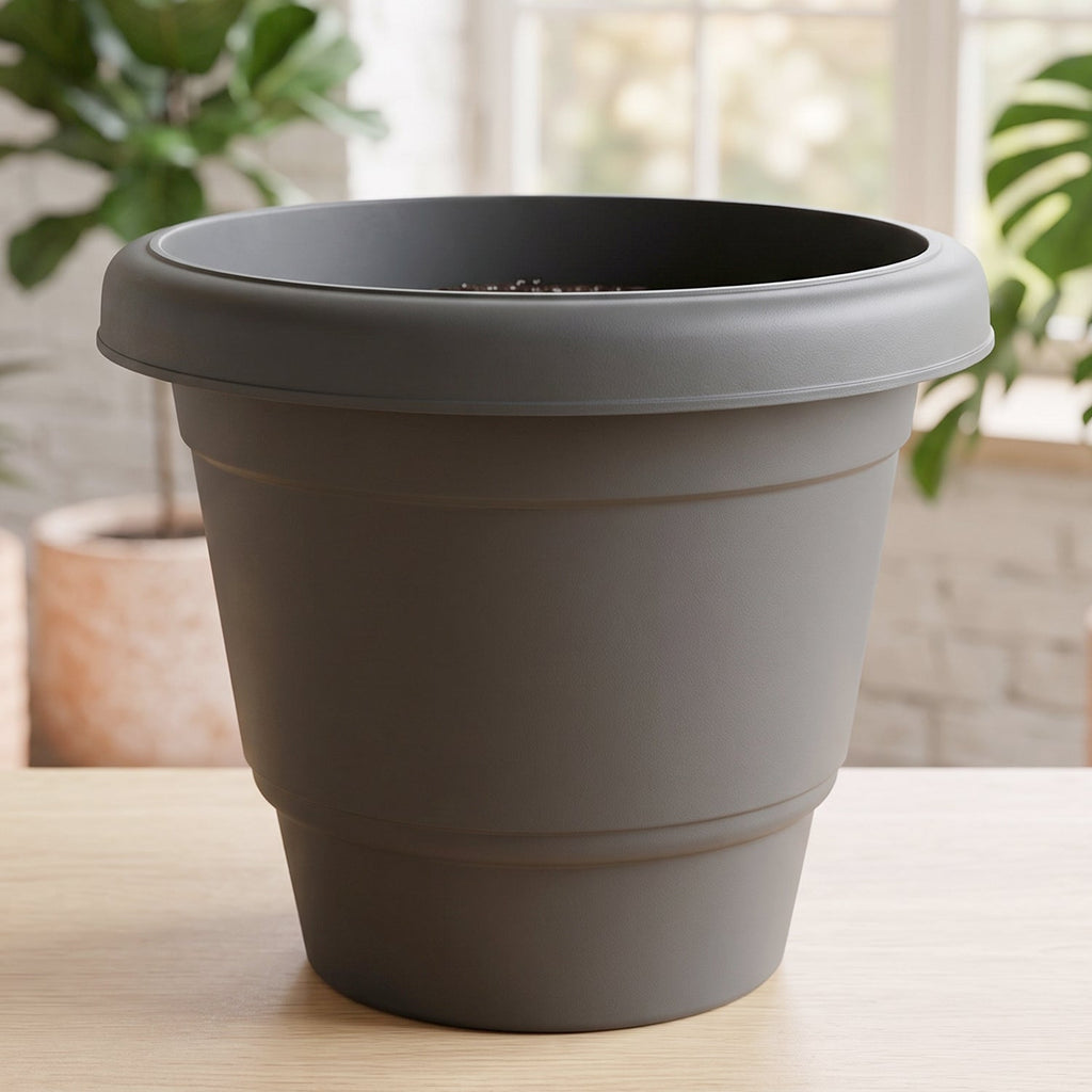 A single empty gray plastic flower pot on a wooden surface, with a blurred green plant in the background.