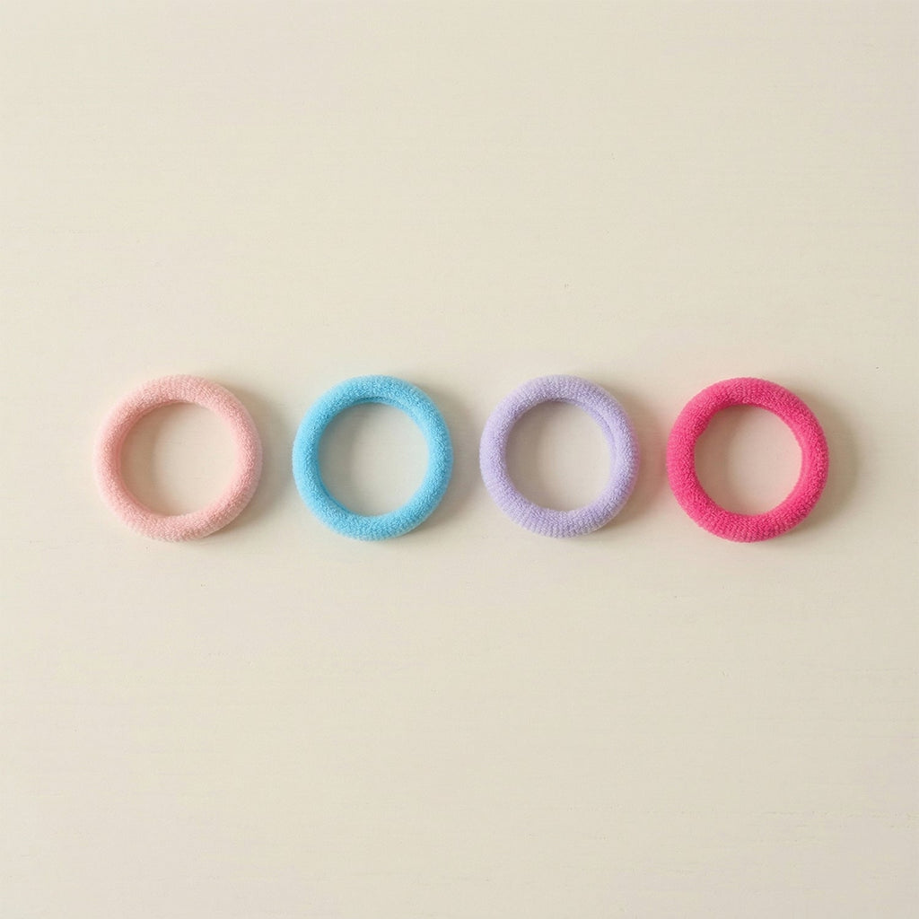 Four colorful elastic hair ties in pink, blue, lavender, and fuchsia arranged in a row on a light beige surface.