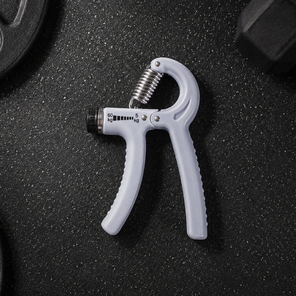 A gray adjustable grip strength trainer with a metal spring lies on a dark gym floor next to a weight plate.