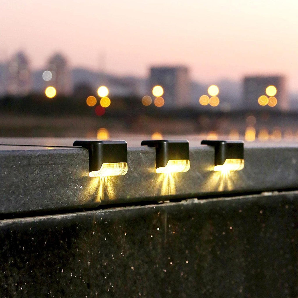 Three black solar lights illuminate a concrete ledge with blurred city lights in the background at dusk.