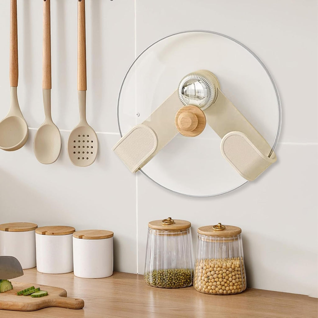 A cream pot lid holder with a wooden knob and chrome center holds a glass lid on a white tiled wall above kitchen counter