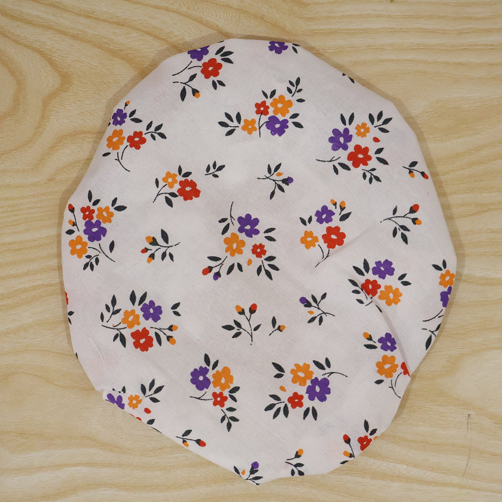 White fabric food cover with a repeating pattern of small red, orange, and purple flowers on wood.