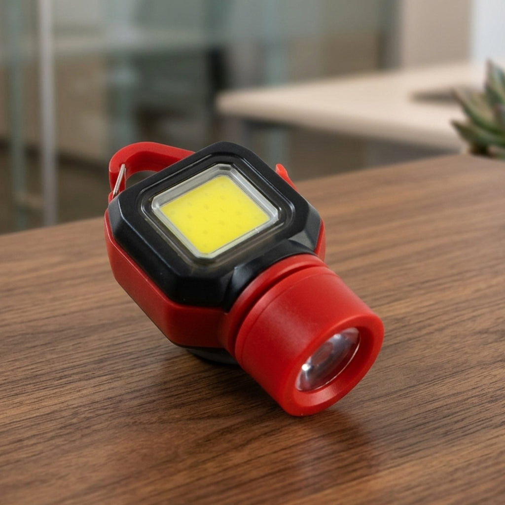 A red and black mini LED flashlight with a carabiner clip resting on a wooden table.