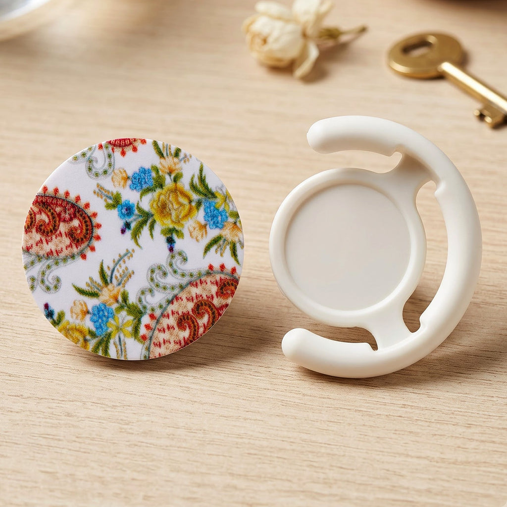 A round pop socket with a white background and colorful paisley floral pattern next to a white plastic car vent – view 9