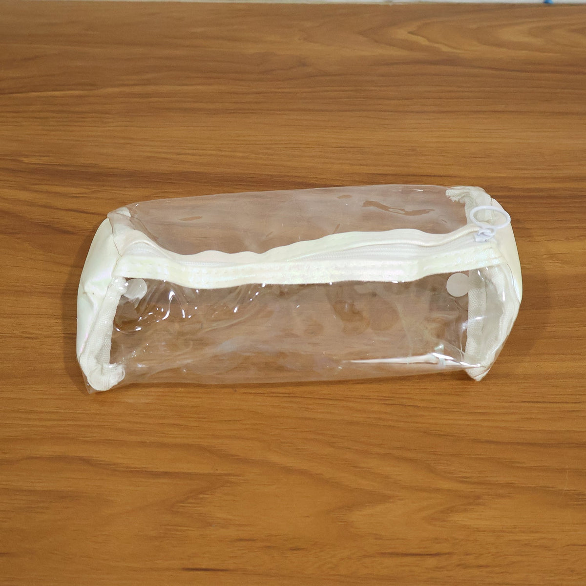 Empty clear PVC pencil case with white trim and zipper, centered on a light brown wooden surface.