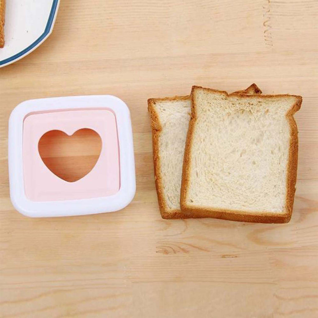 Pink and white heart-shaped sandwich cutter next to two slices of white bread on a wooden table.