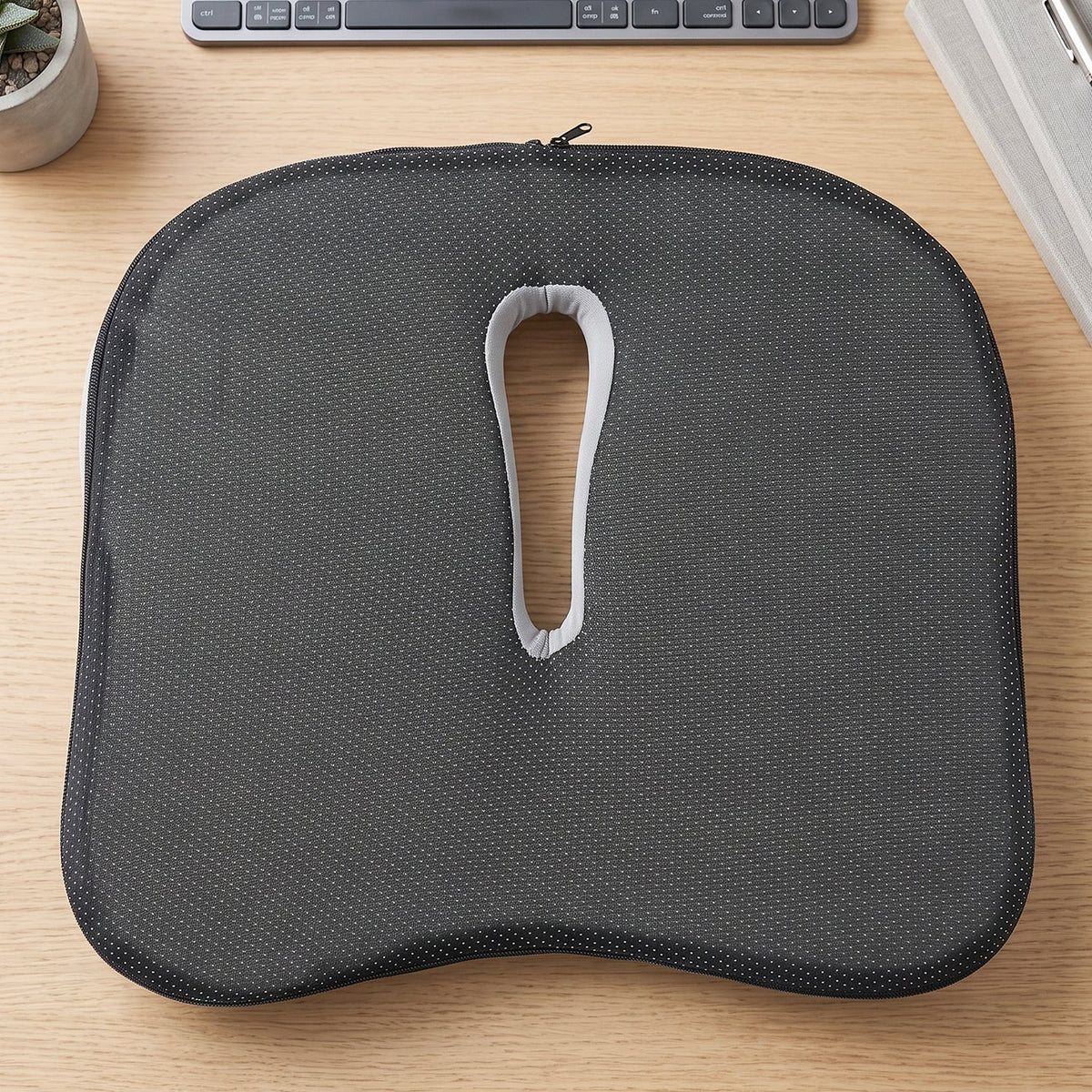 Bottom view of the dark grey, anti-slip ergonomic seat cushion with a central cutout and zipper.