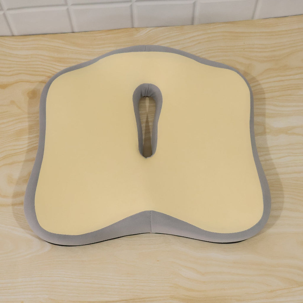 A beige and grey ergonomic seat cushion resting on a light wooden surface.