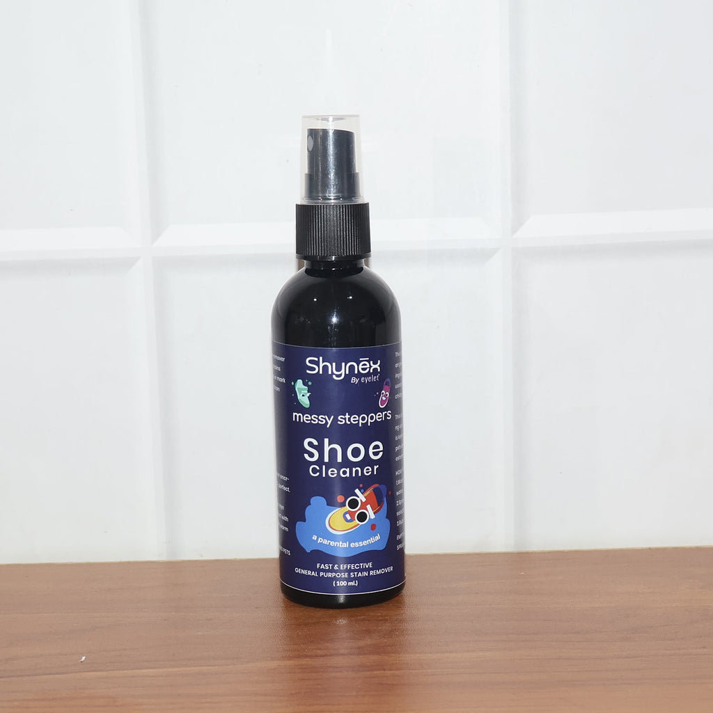 A Shynex shoe cleaner bottle with a clear cap stands on a wooden surface against a white tiled wall.