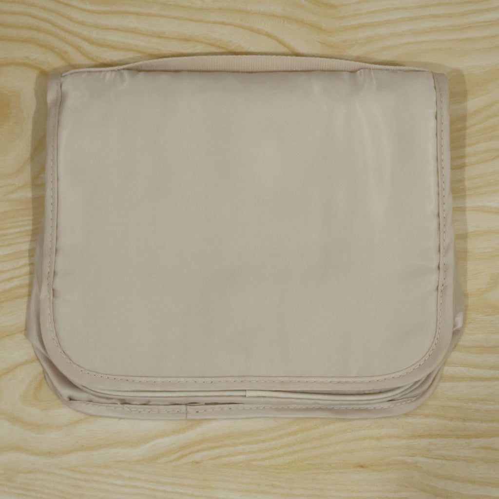 A neatly folded beige toiletry bag with a subtle sheen, resting on a light wooden background.