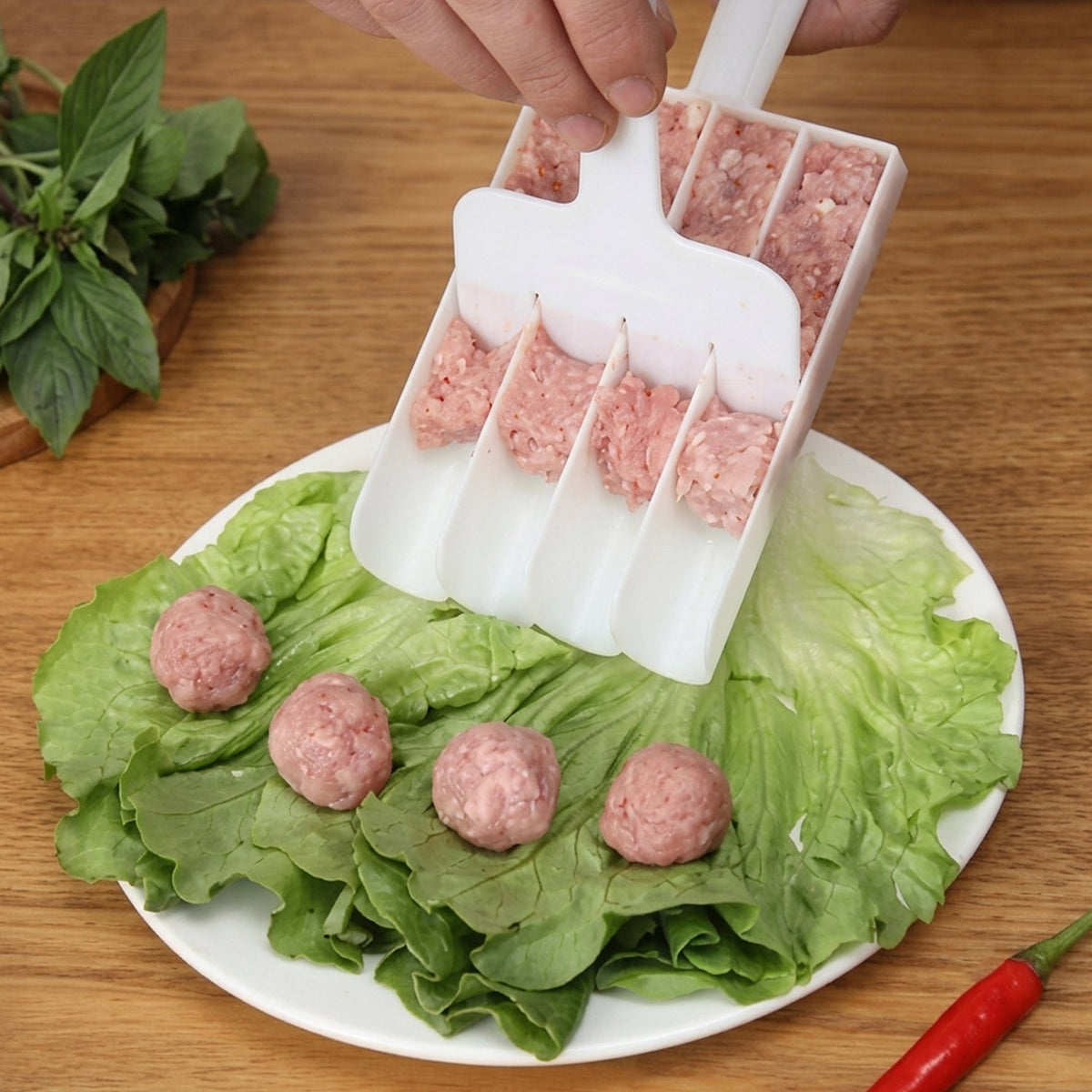 A person uses a white plastic meatball maker to scoop raw ground meat onto a bed of green lettuce on a white plate.