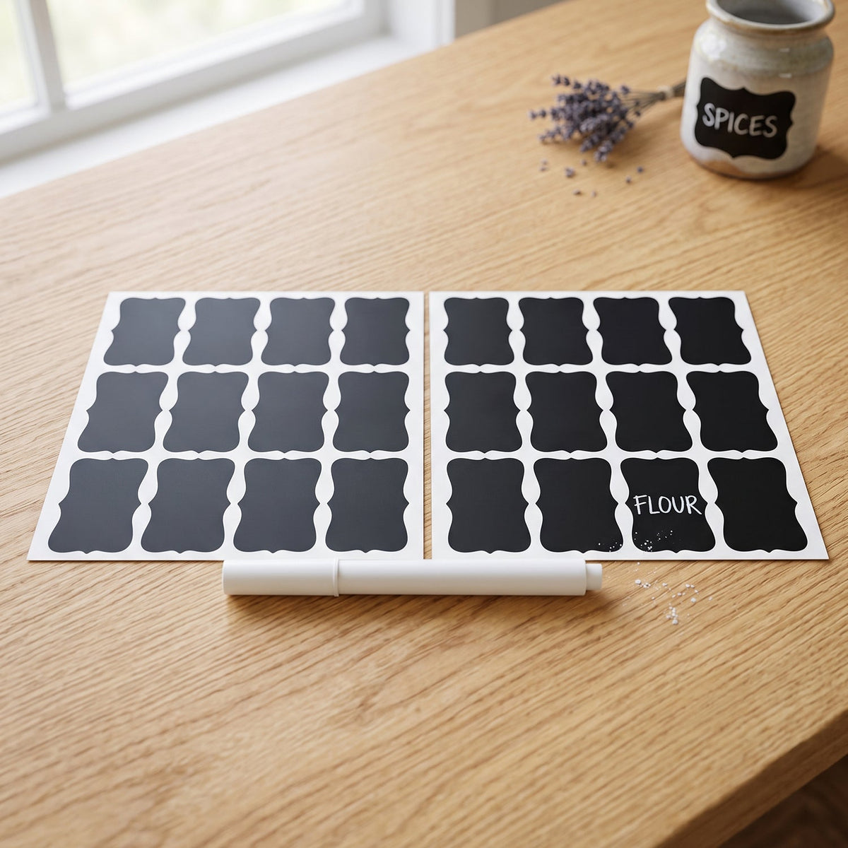 Two sheets of blank chalkboard labels and a white marker on a wooden table, with a small jar labeled "SPICES".