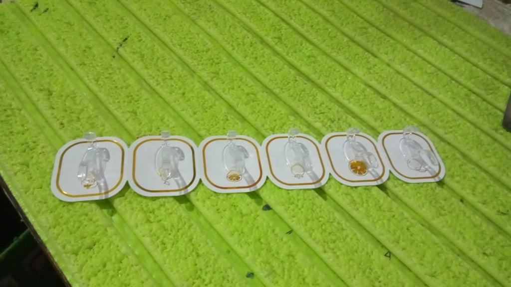 Six transparent adhesive hooks with gold borders laid out on a textured green surface.