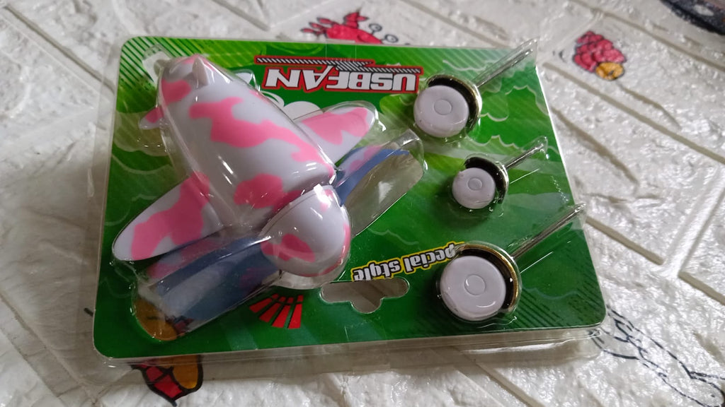 The pink and white airplane USB fan and its three wheels are sealed in clear plastic packaging with a green backing.