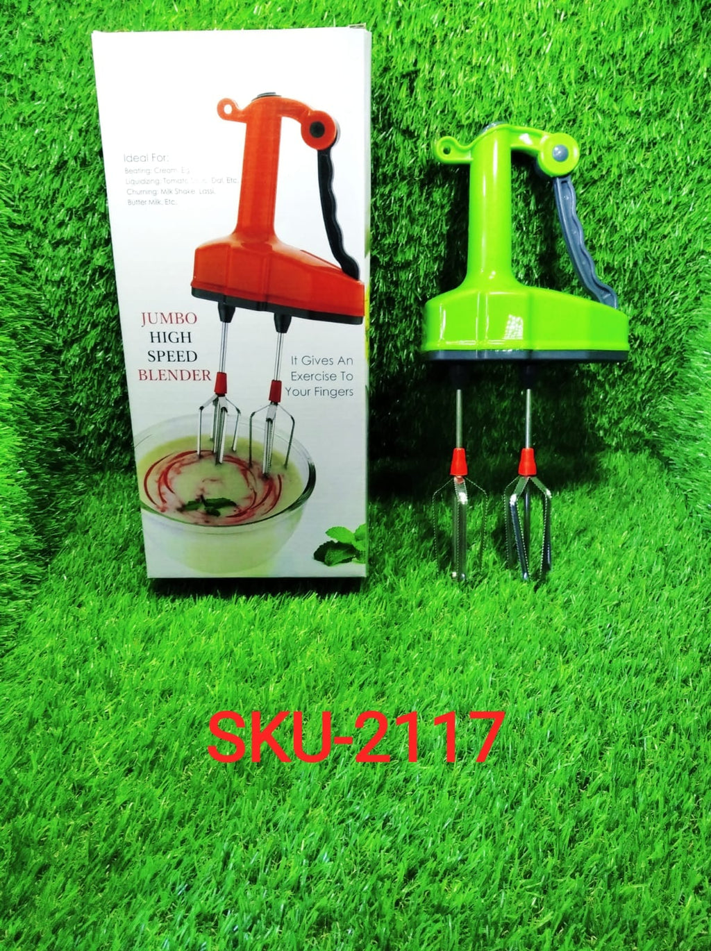 A green manual hand blender with whisks sits on artificial grass next to its white product box, which features an orange