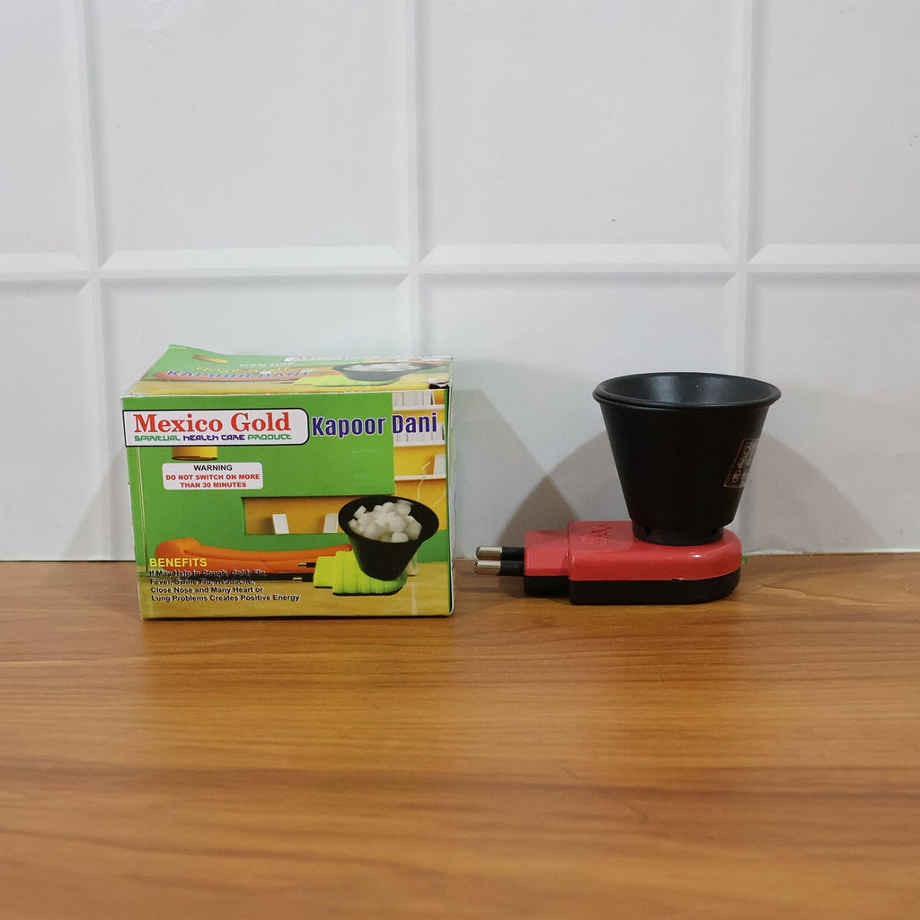 A red and black electric Kapoor Dani diffuser next to its green and yellow product packaging on a wooden surface.