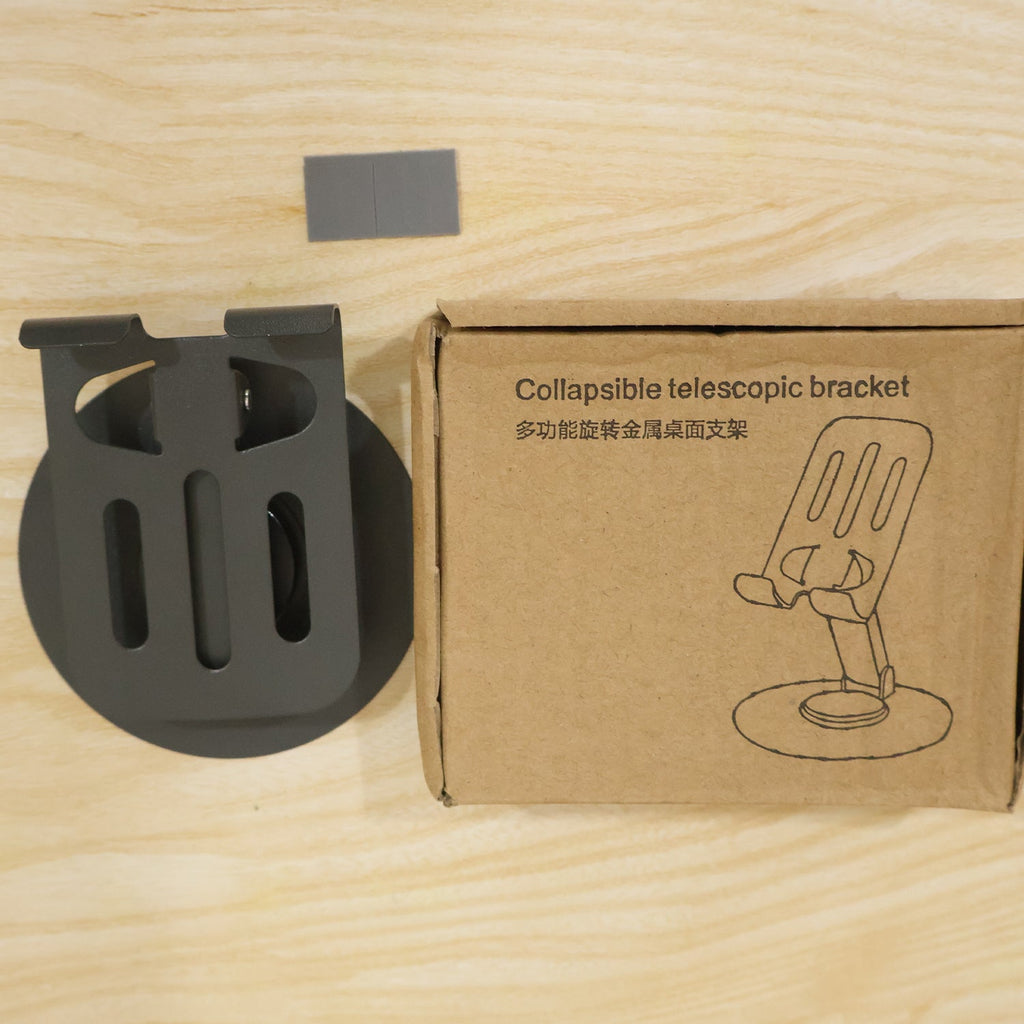 A black metal mobile stand next to its brown cardboard box labeled "Collapsible telescopic bracket" on a wooden surface.