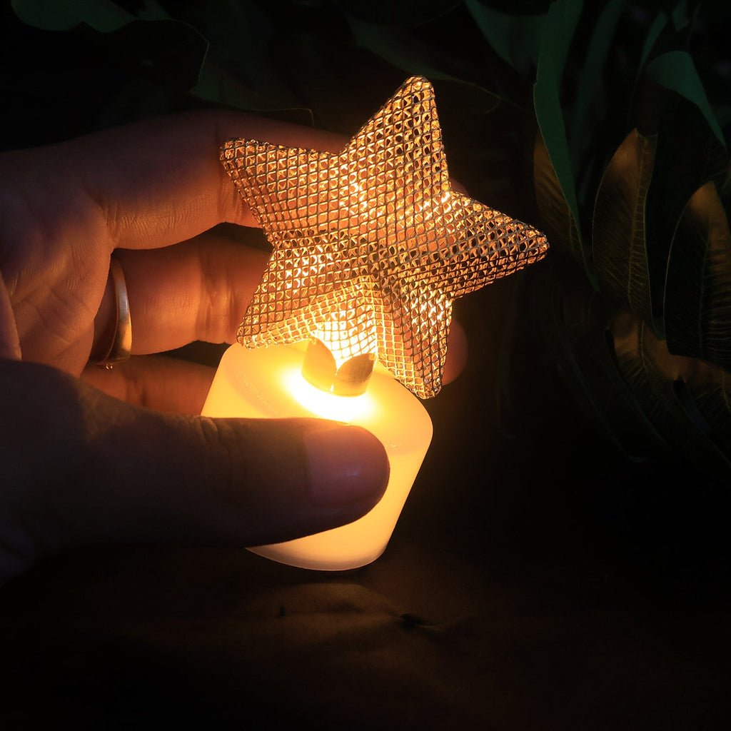 A hand holding a single glowing LED tealight with a golden mesh star in a dimly lit setting.